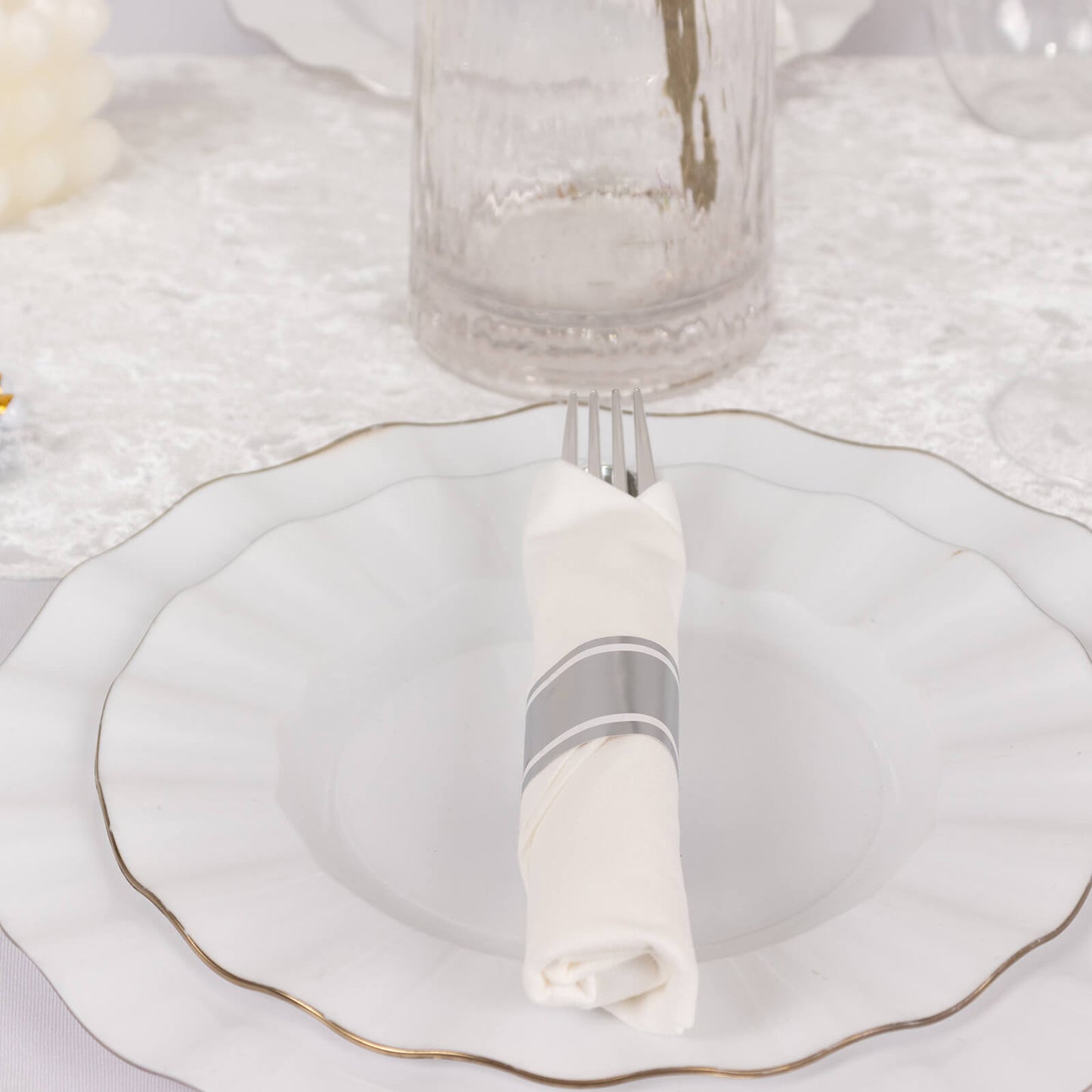 Set of silver disposable cutlery with white napkins on a decorative plate.