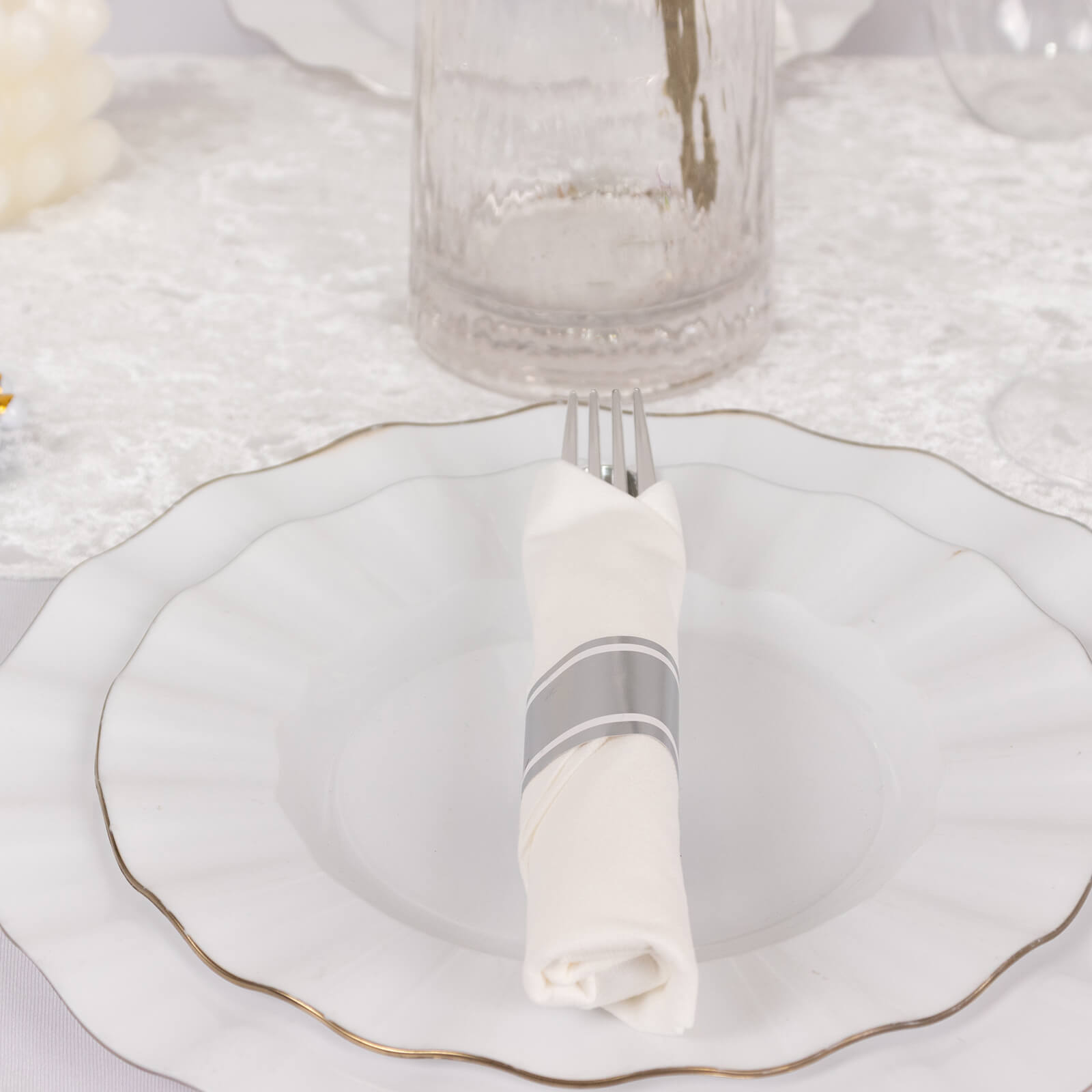 Set of silver disposable cutlery with white napkins on a decorative plate.