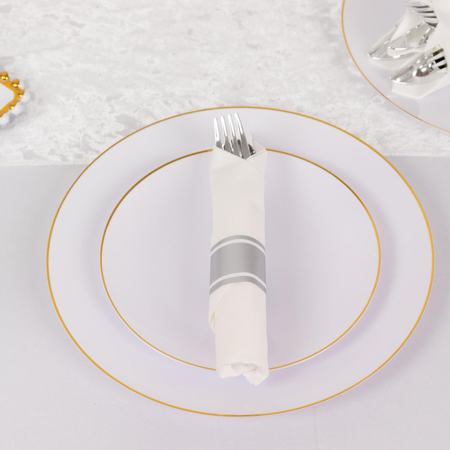 Silver pre-rolled cutlery set with white napkins on a plate.