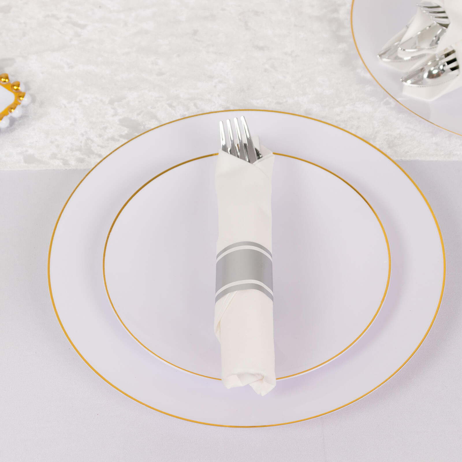 Silver pre-rolled cutlery set with white napkins on a plate.