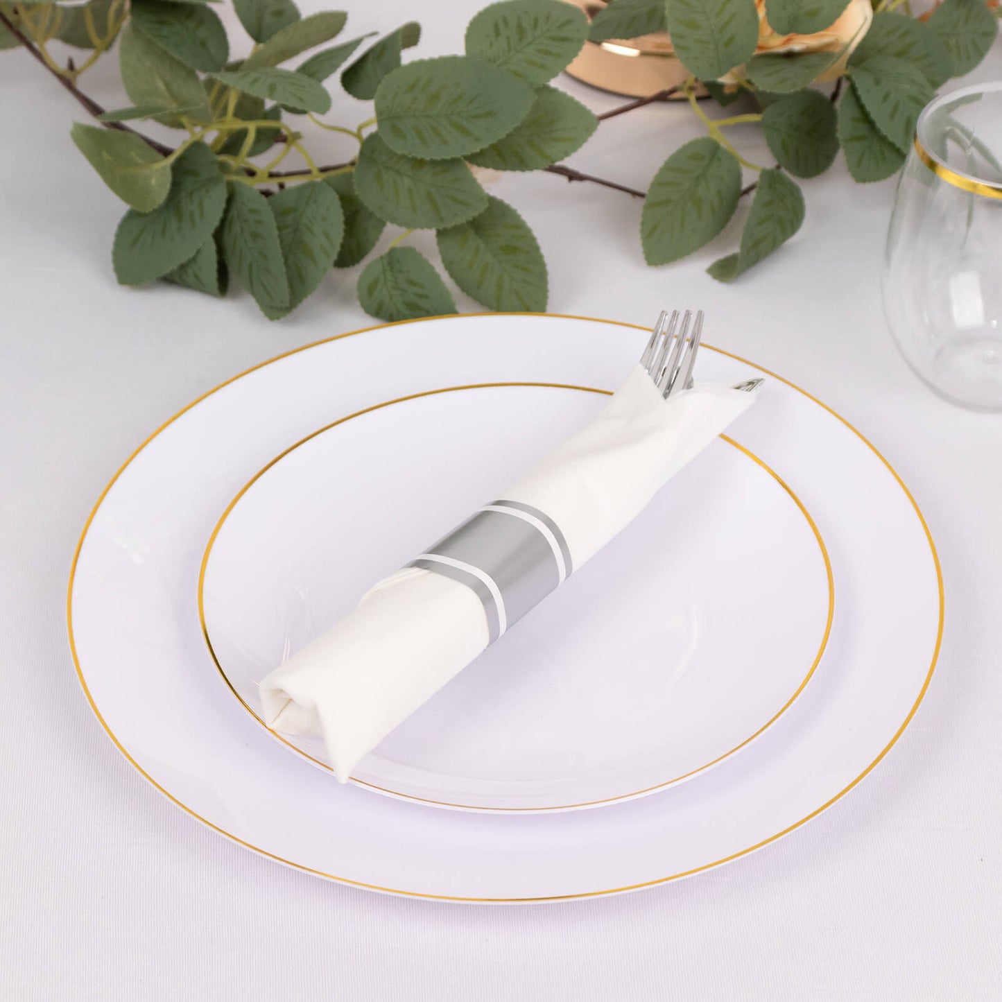 Silver disposable cutlery set with white napkins on a decorative plate.