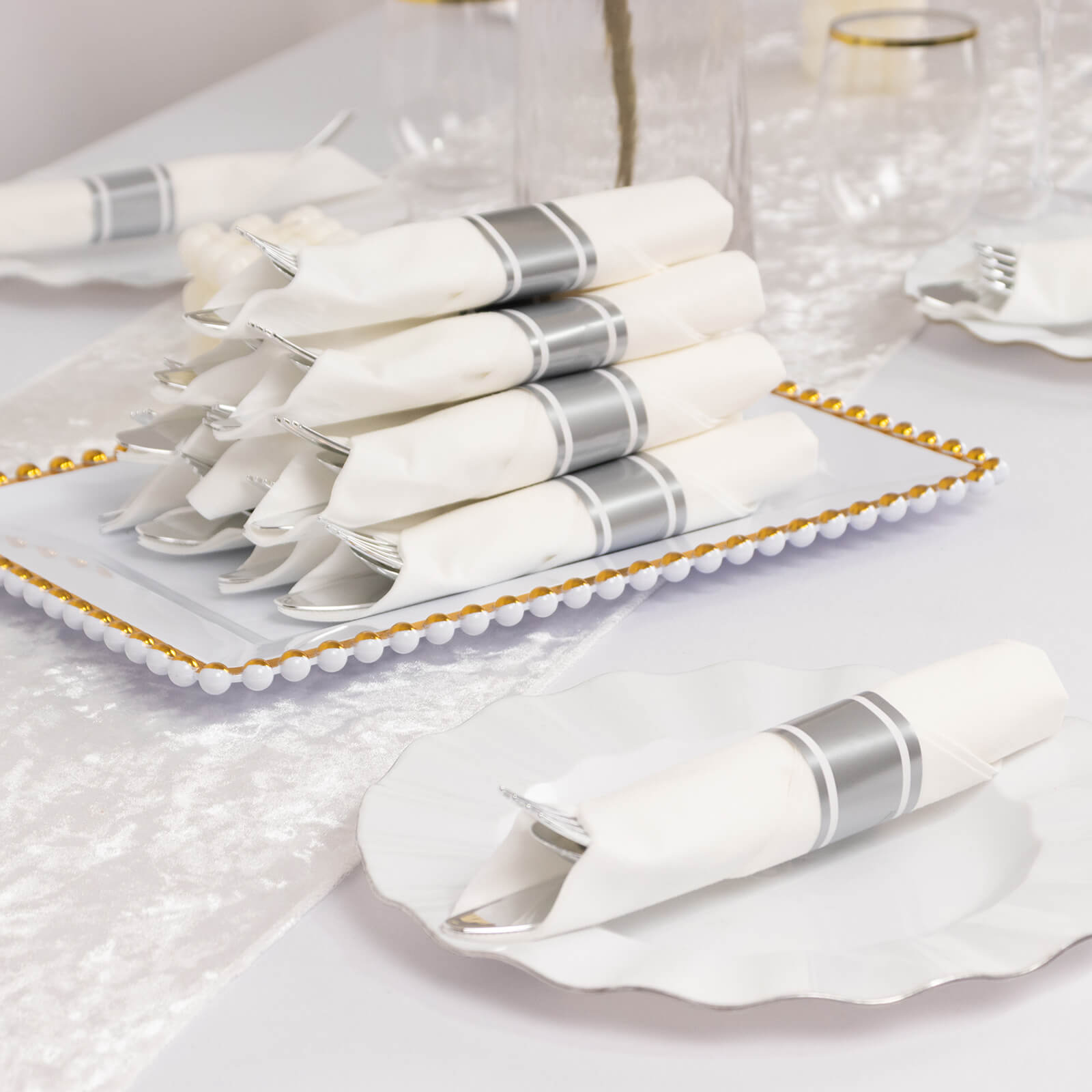 Silver disposable cutlery set with white napkins on a decorative tray.