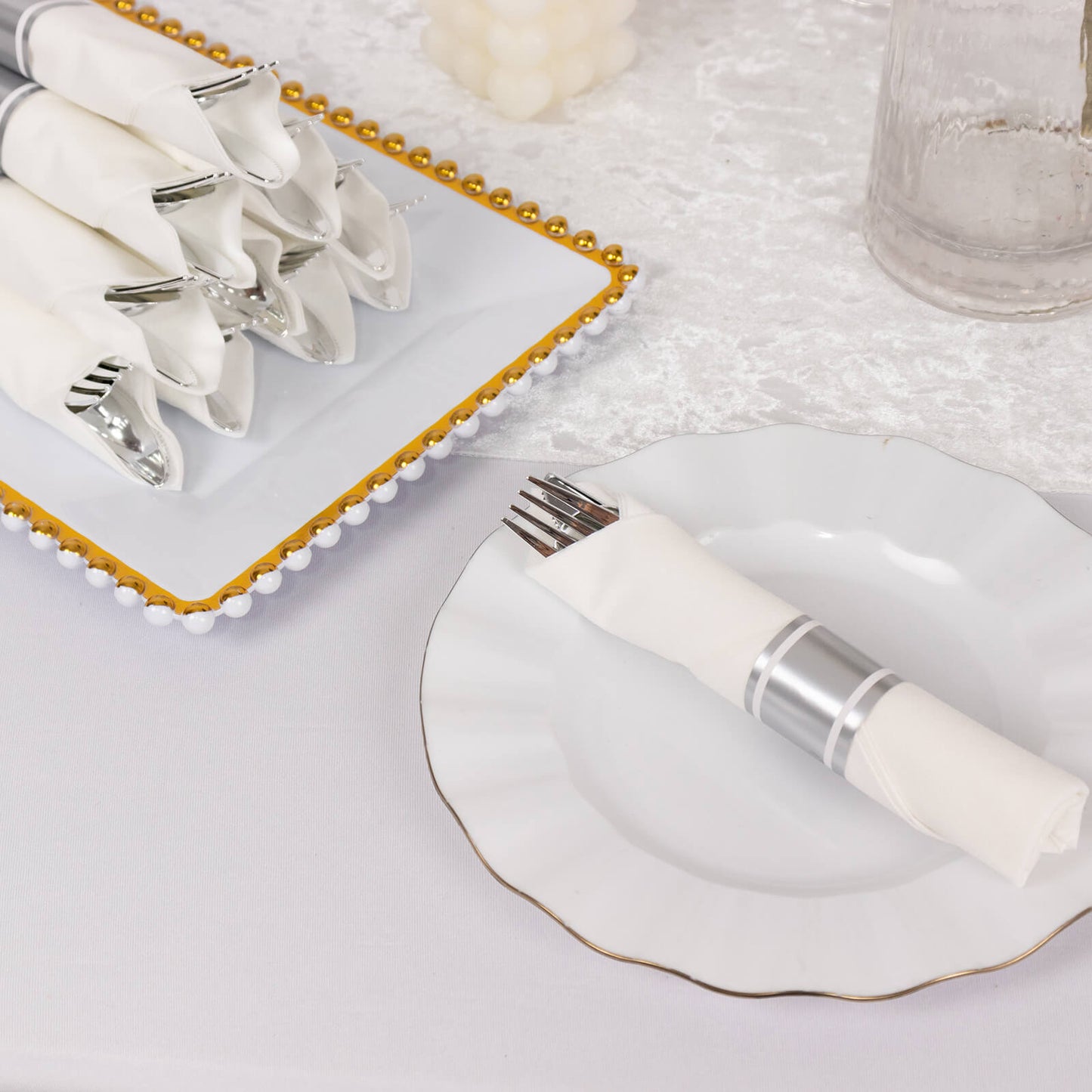 Set of silver disposable cutlery with white napkins on a table setting.