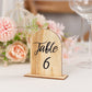 Natural rustic wooden table number 6 in arch shape, surrounded by flowers.