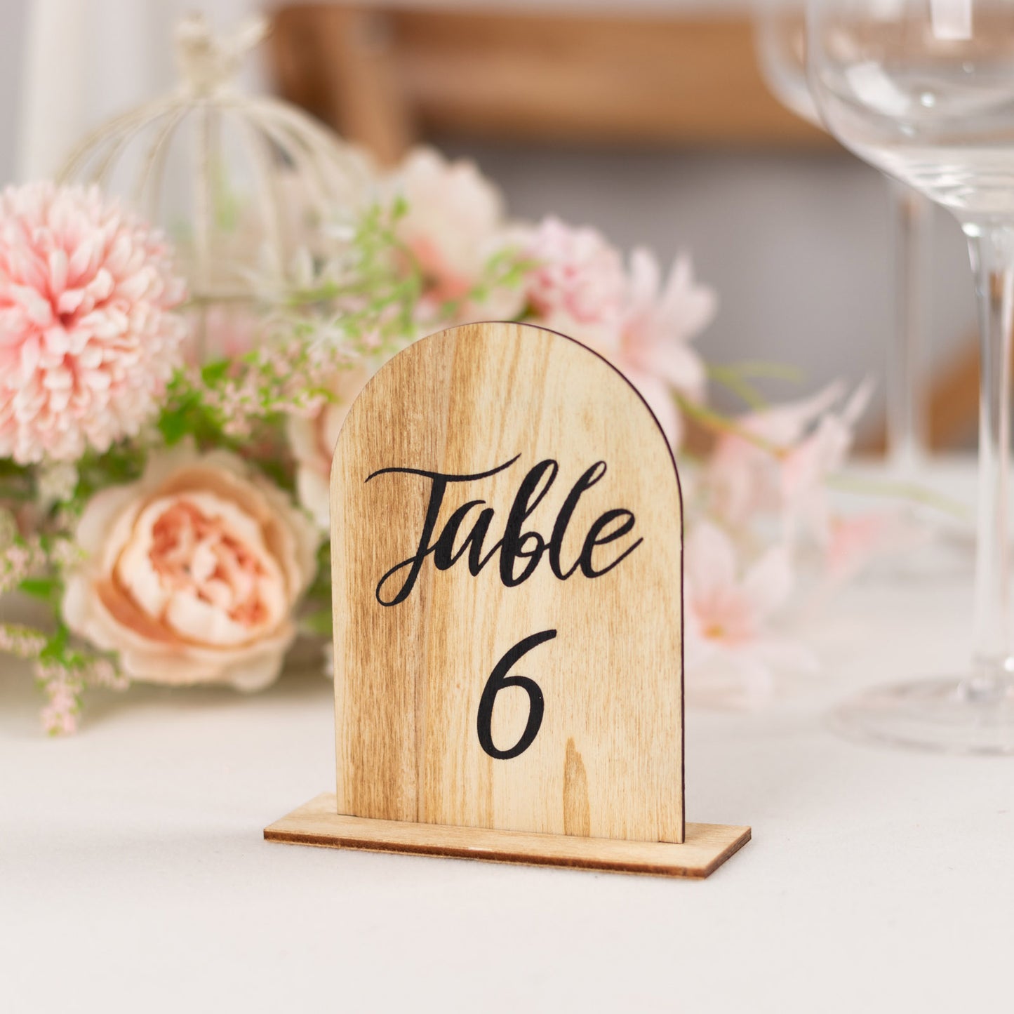 Natural rustic wooden table number 6 in arch shape, surrounded by flowers.