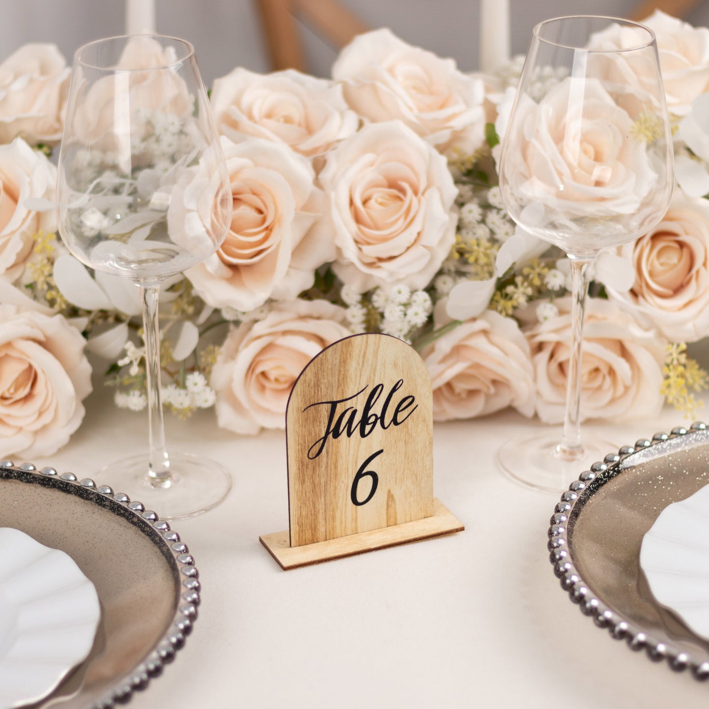 Natural wood table number 6 surrounded by blush roses at an elegant event setting.
