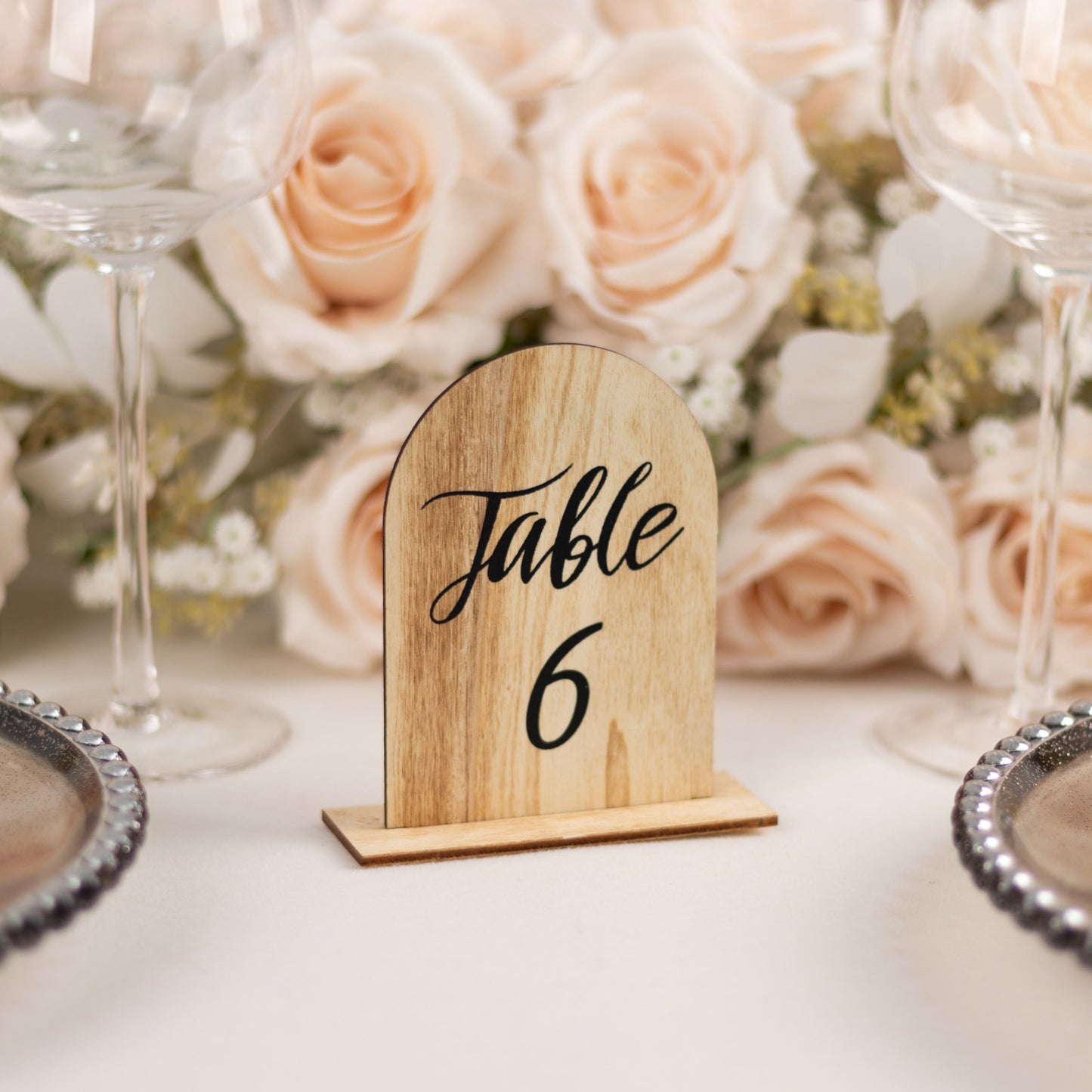 Natural rustic wooden arch table number 6 with flowers and glassware in the background.