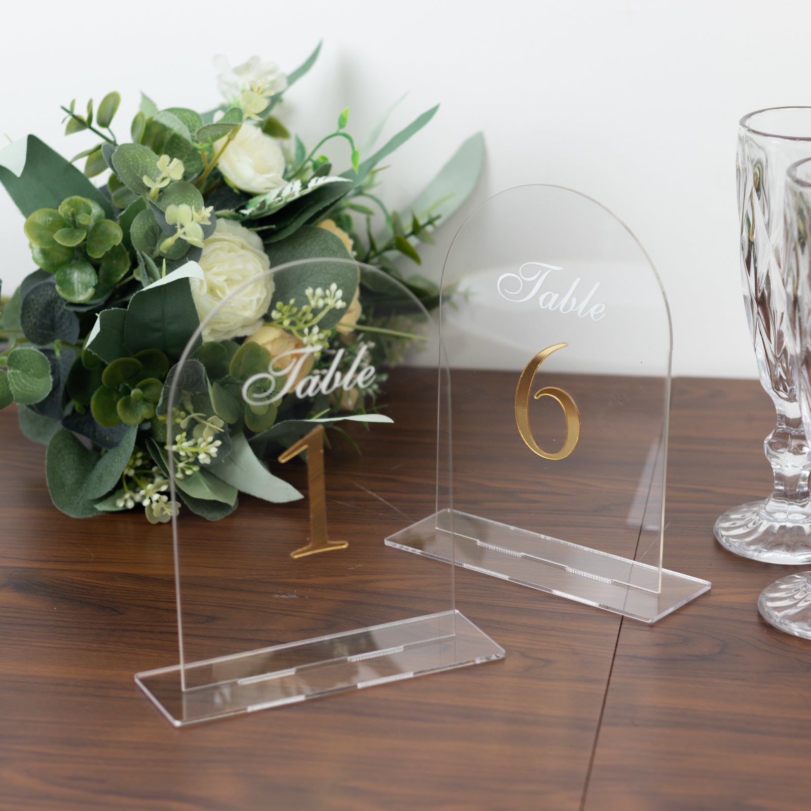 Clear arch acrylic table numbers with gold print on a wooden table.