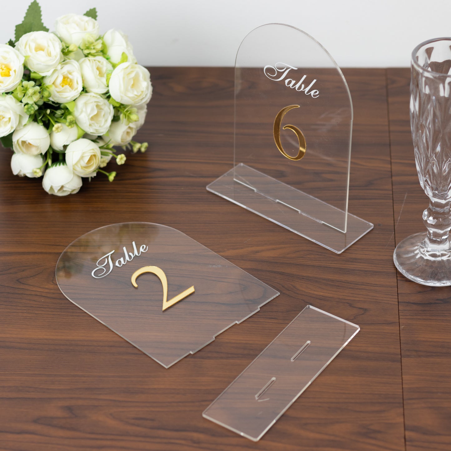 Clear arch acrylic table numbers with gold print on a wooden table.