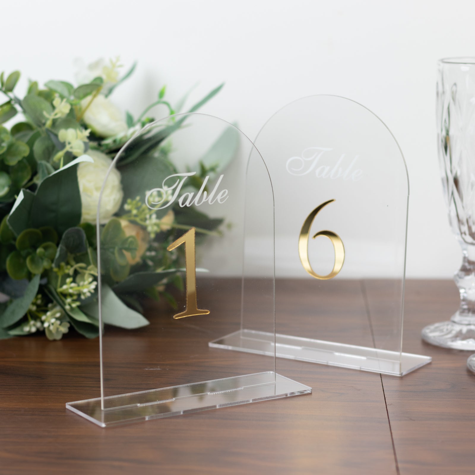 Clear arch acrylic table numbers with gold print on a wooden table.