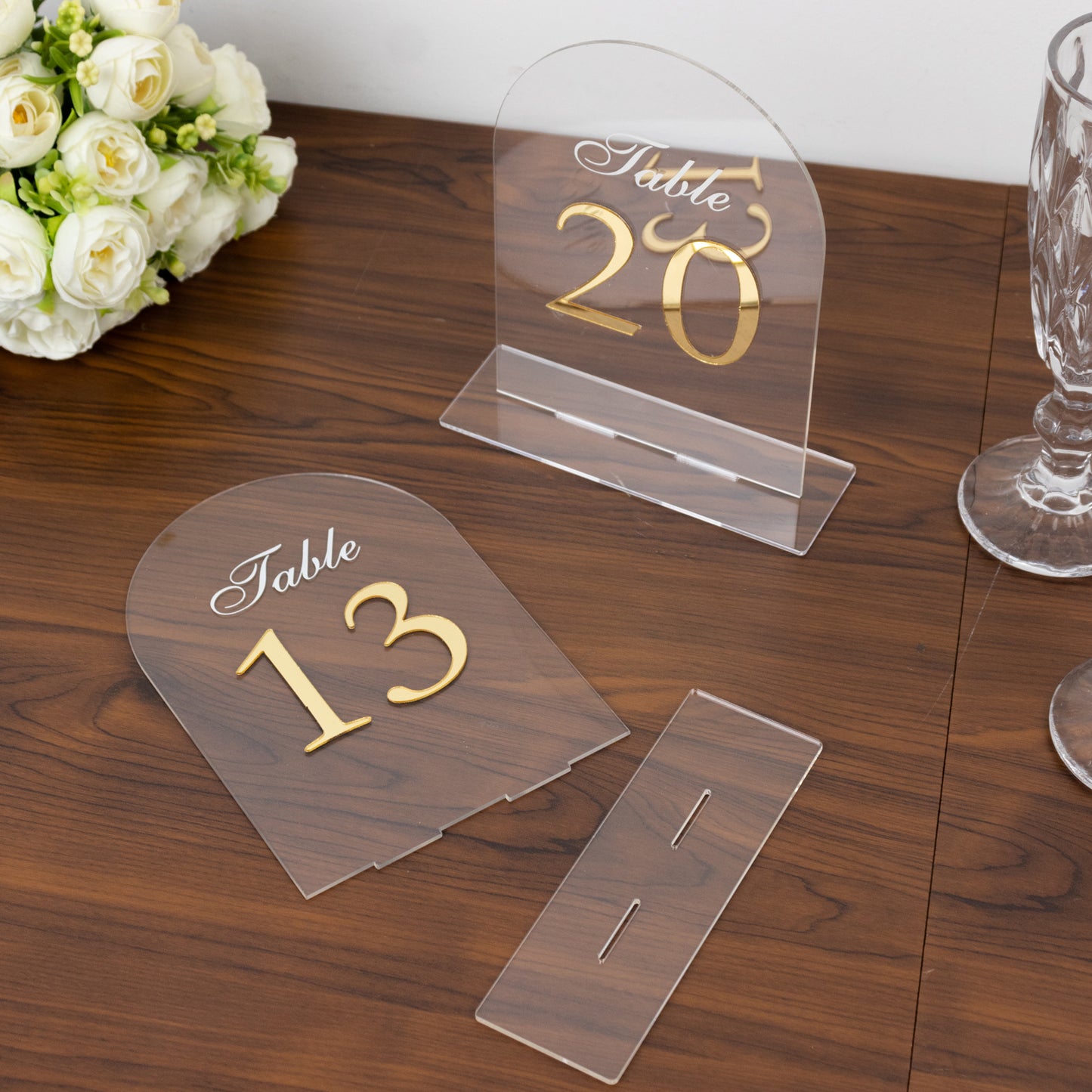 Clear arch acrylic table numbers with gold print on a wooden table.