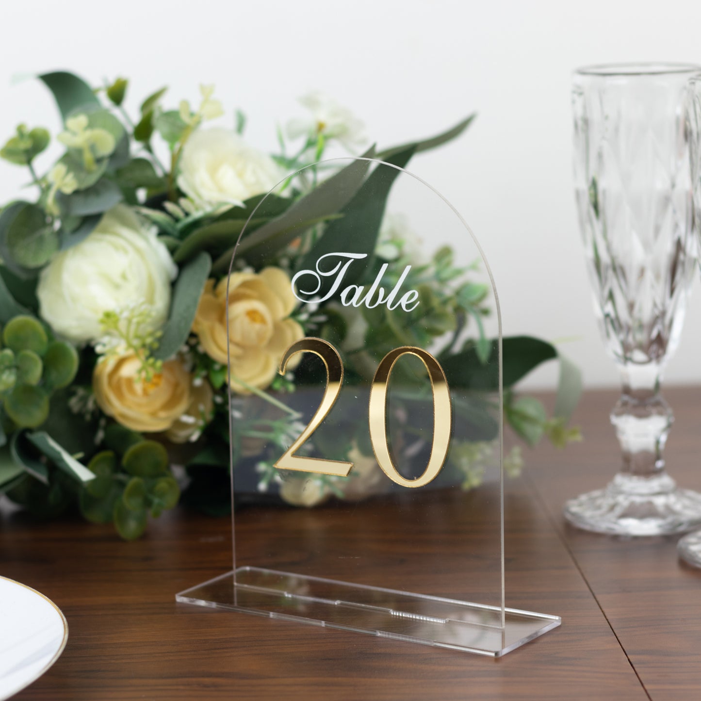 Clear arch acrylic table number with gold print, set on a wooden table.