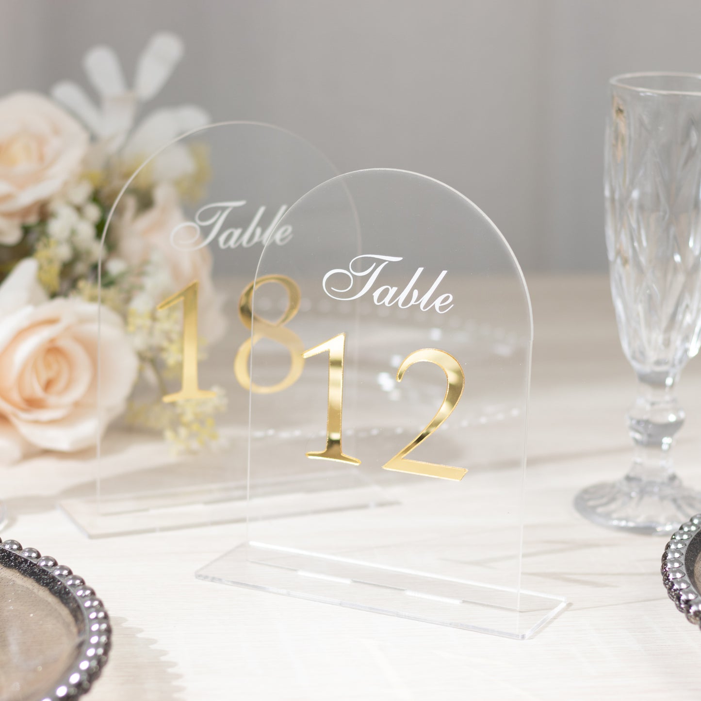 Clear arch acrylic table numbers with gold print on a light background.