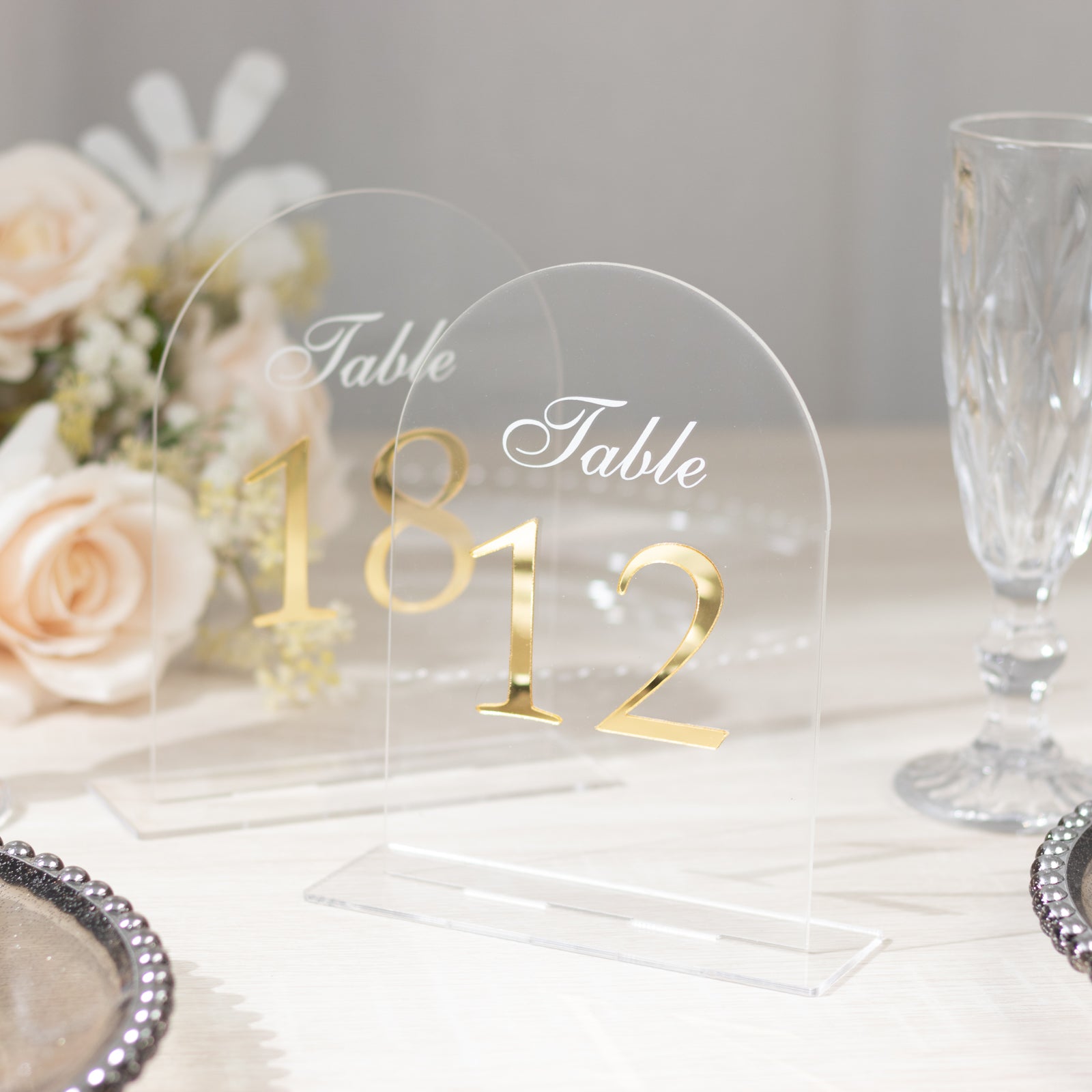 Clear arch acrylic table numbers with gold print on a light background.