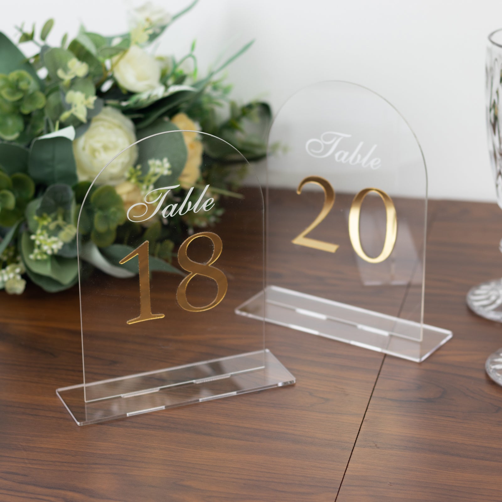 Clear arch acrylic table numbers with gold print on a wooden table.