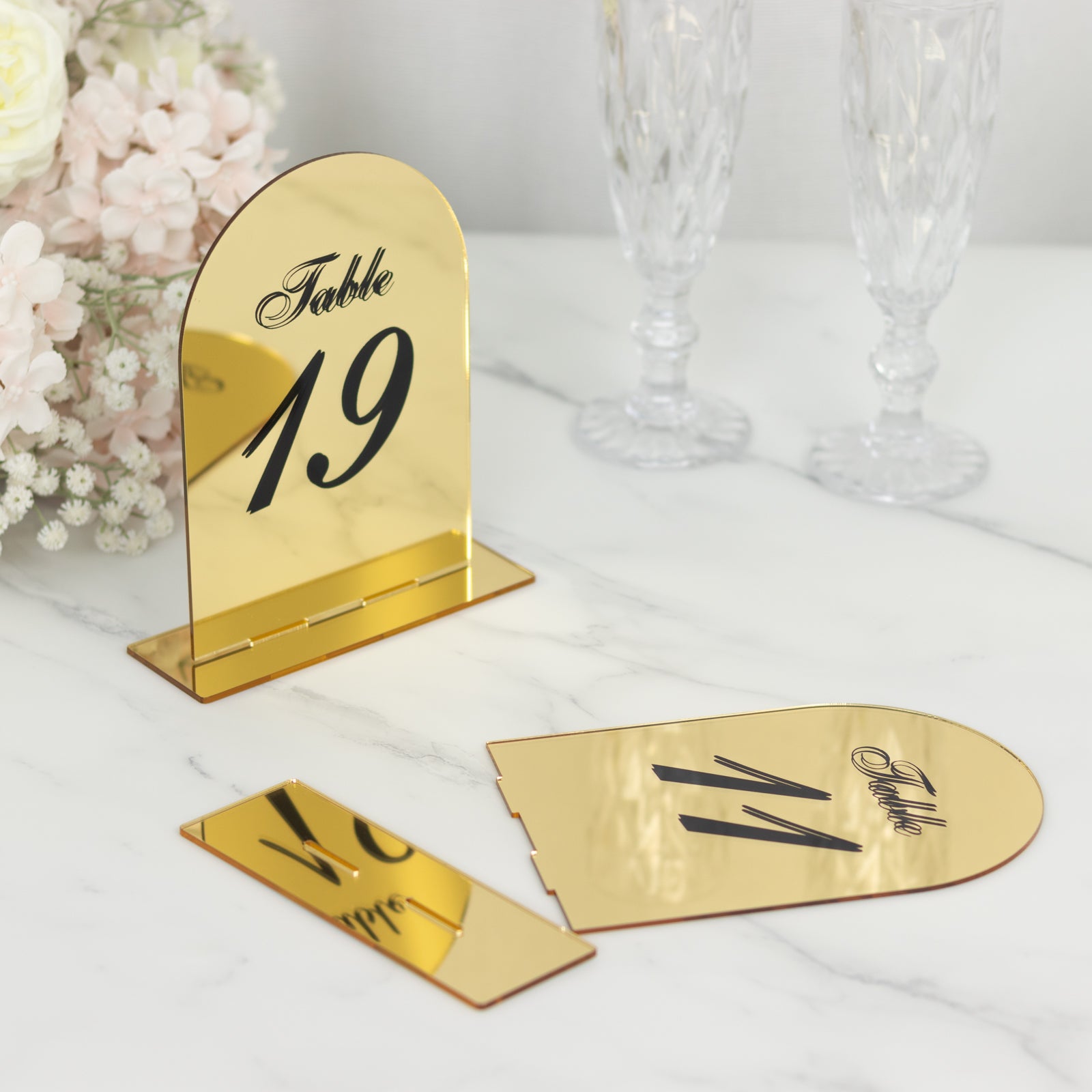 Gold mirror arch table number 19 with black print on a marble surface.