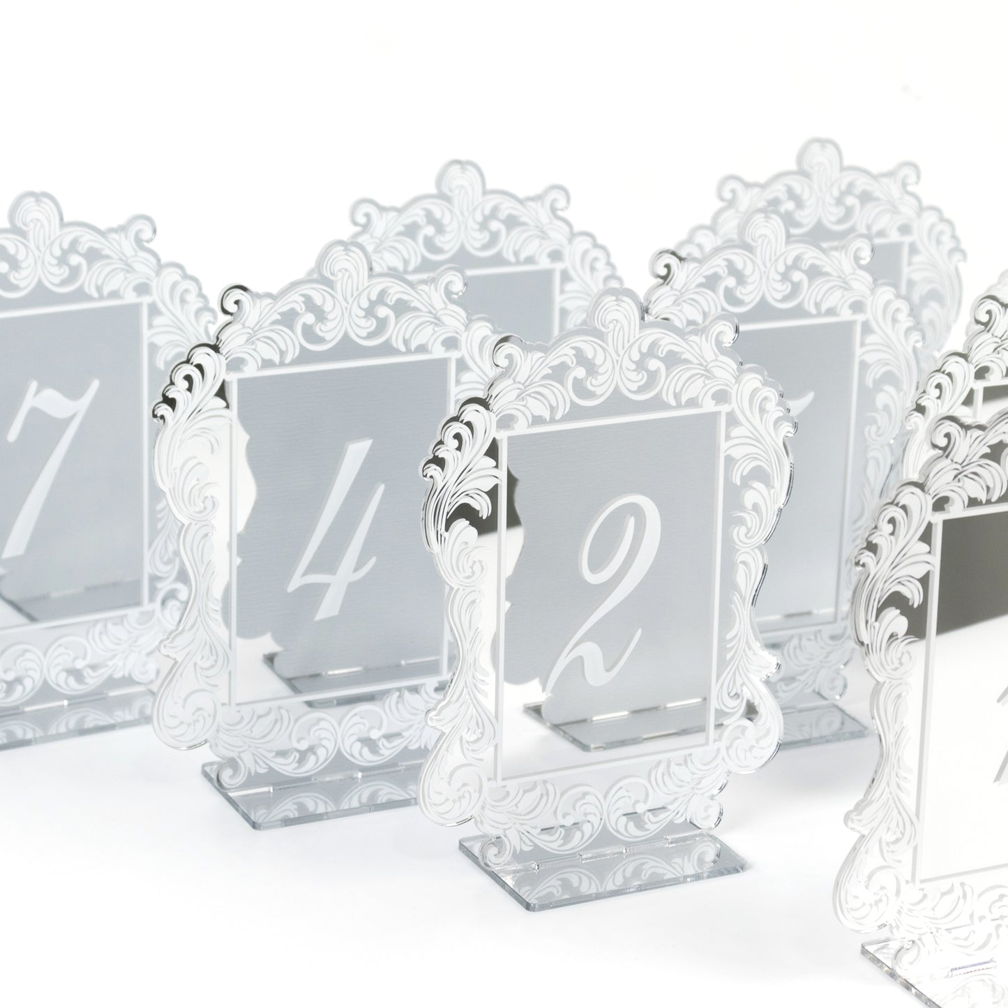 Silver mirror table numbers with baroque lace border, white print, and stands.