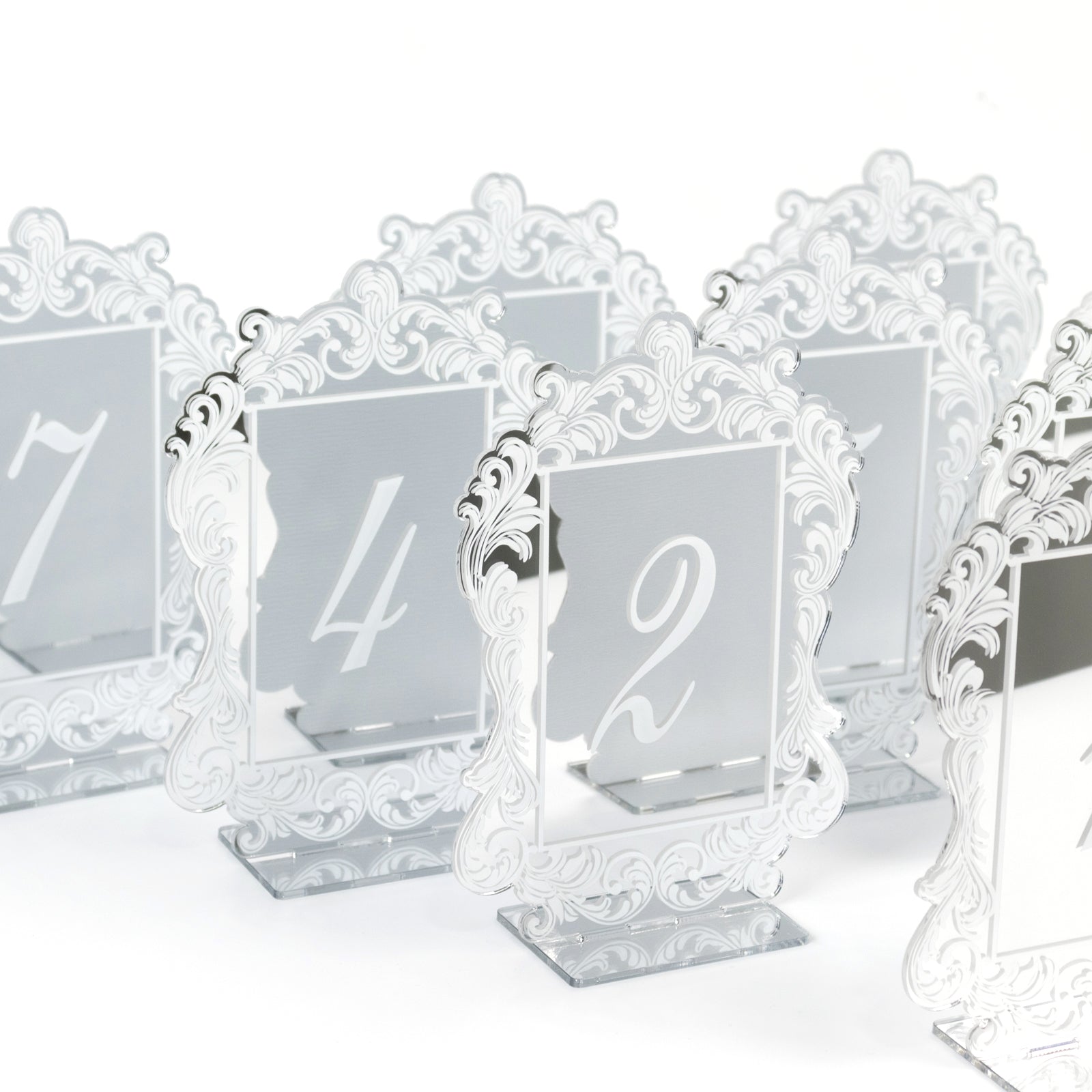 Silver mirror table numbers with baroque lace border, white print, and stands.
