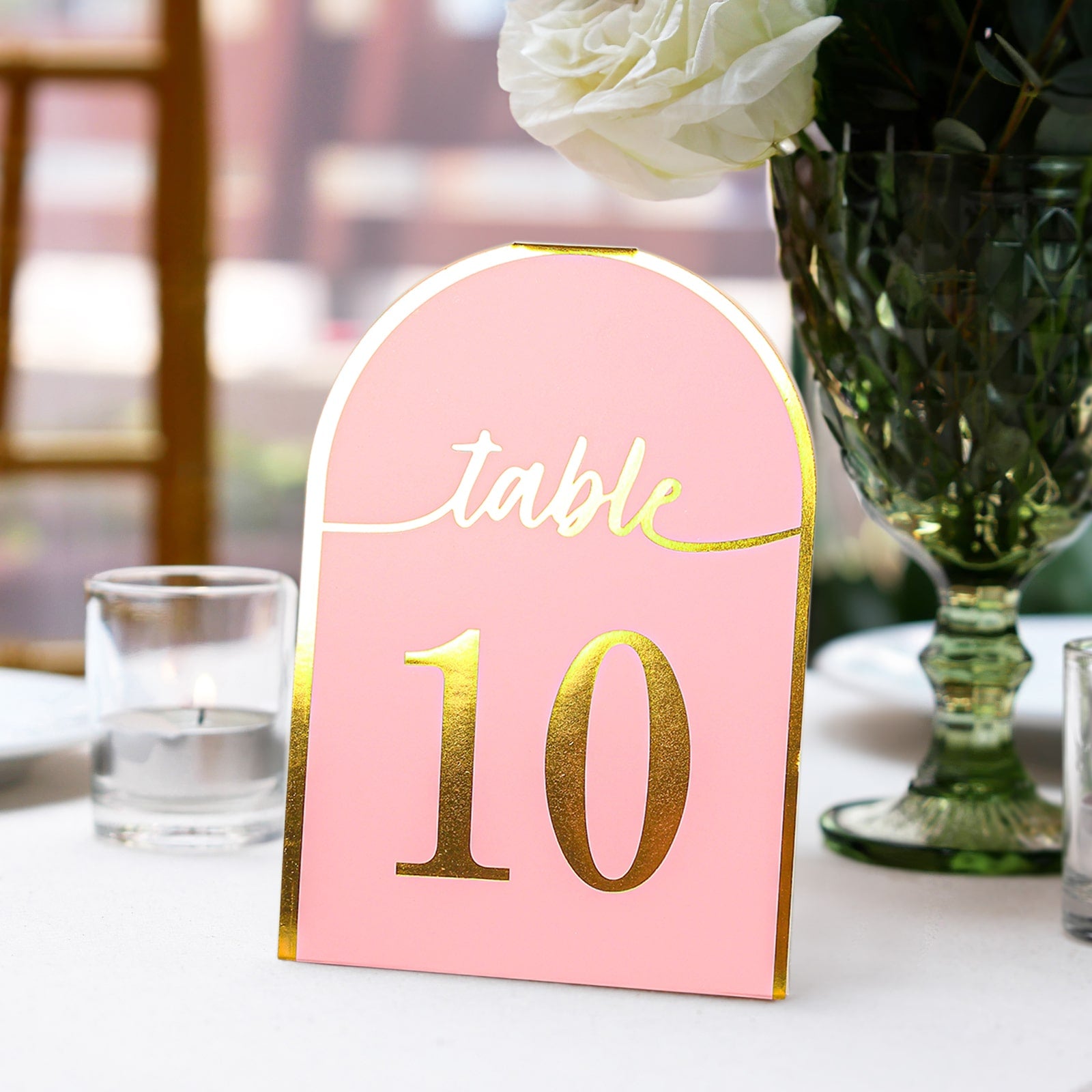 Blush pink disposable table number with gold foil, standing on a table setting.