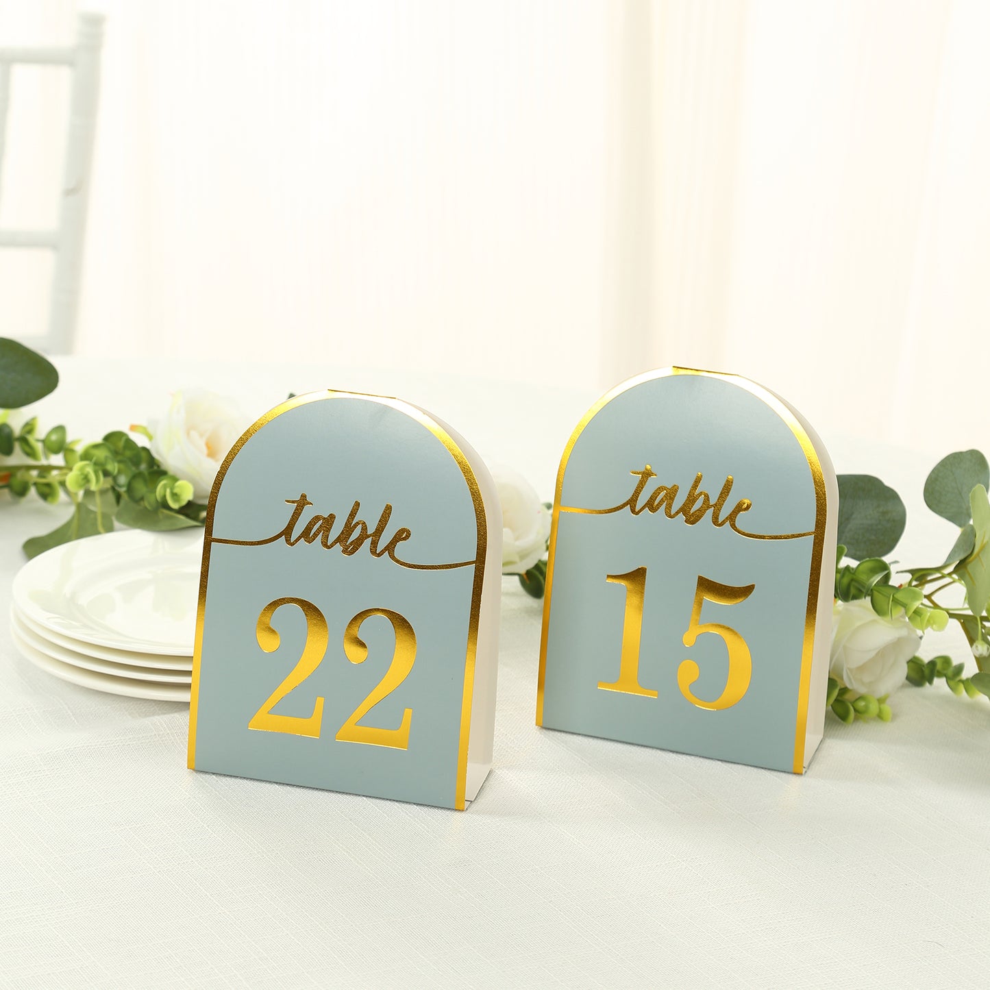 Dusty blue table numbers with gold foil, standing on a table setting.
