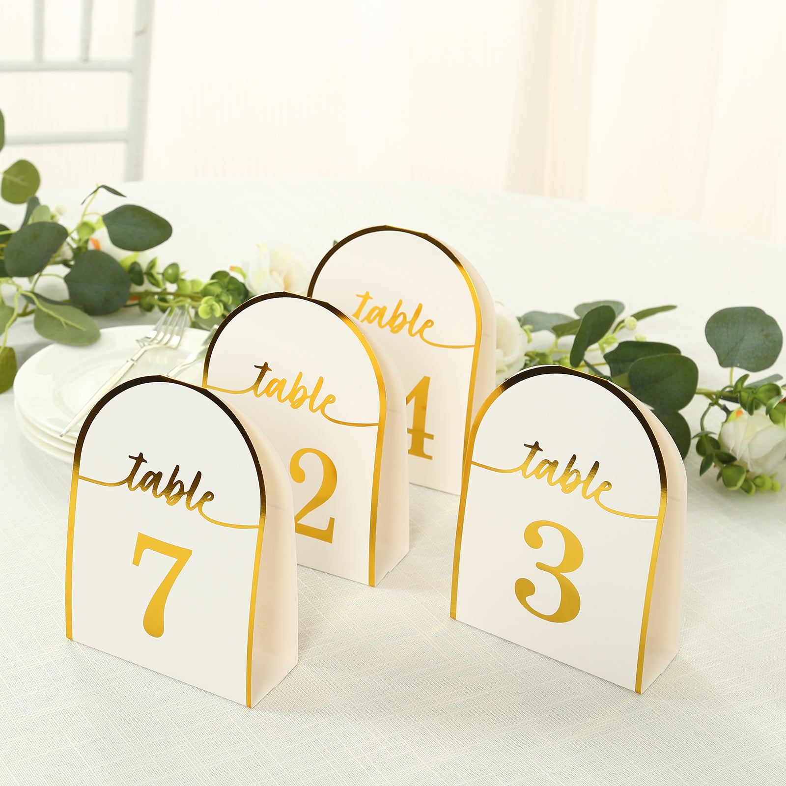 White and gold table numbers, double-sided, numbered 1-7, set on a table.