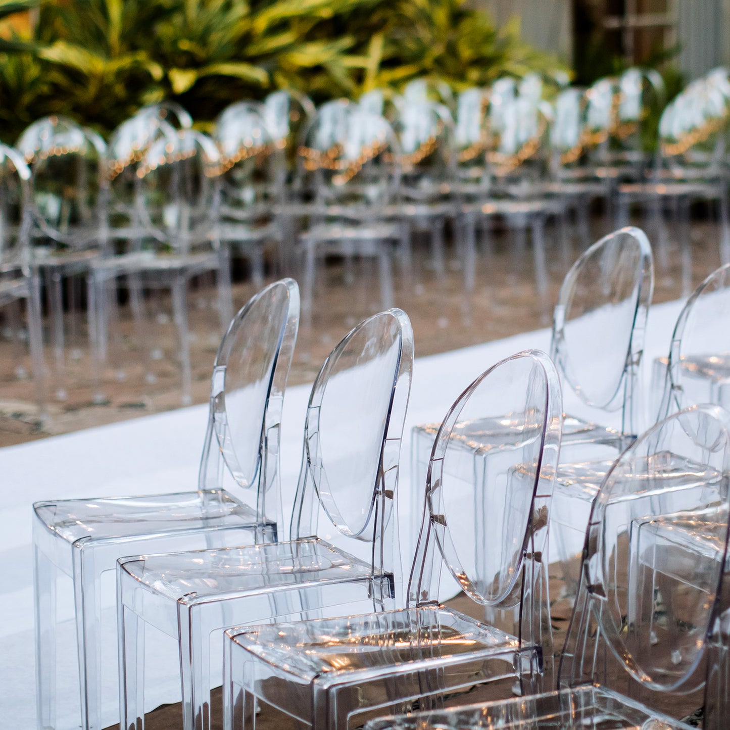 Clear acrylic ghost banquet chairs with oval backs, fully assembled, in an outdoor setting.