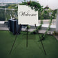 Black metal easel stand holding a welcome sign at an event.