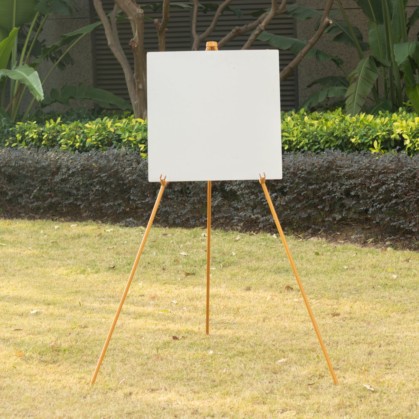 Gold metal easel stand for signs and art in a garden setting.