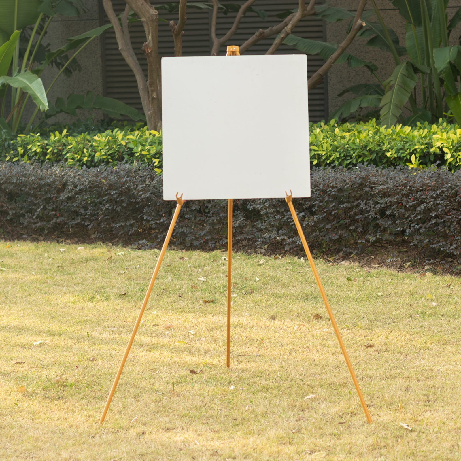 Gold metal easel stand for signs and art in a garden setting.