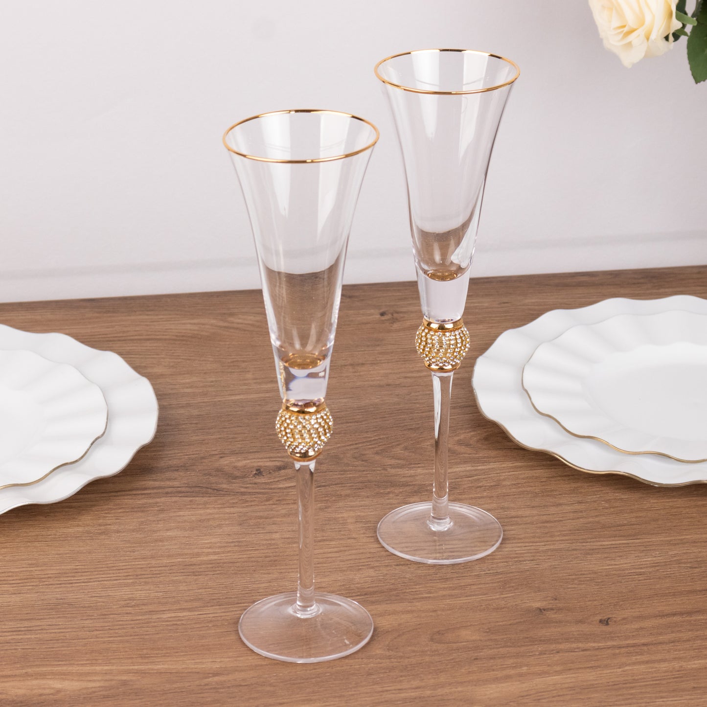 Gold rim crystal champagne flutes with studded rhinestones on a wooden table.