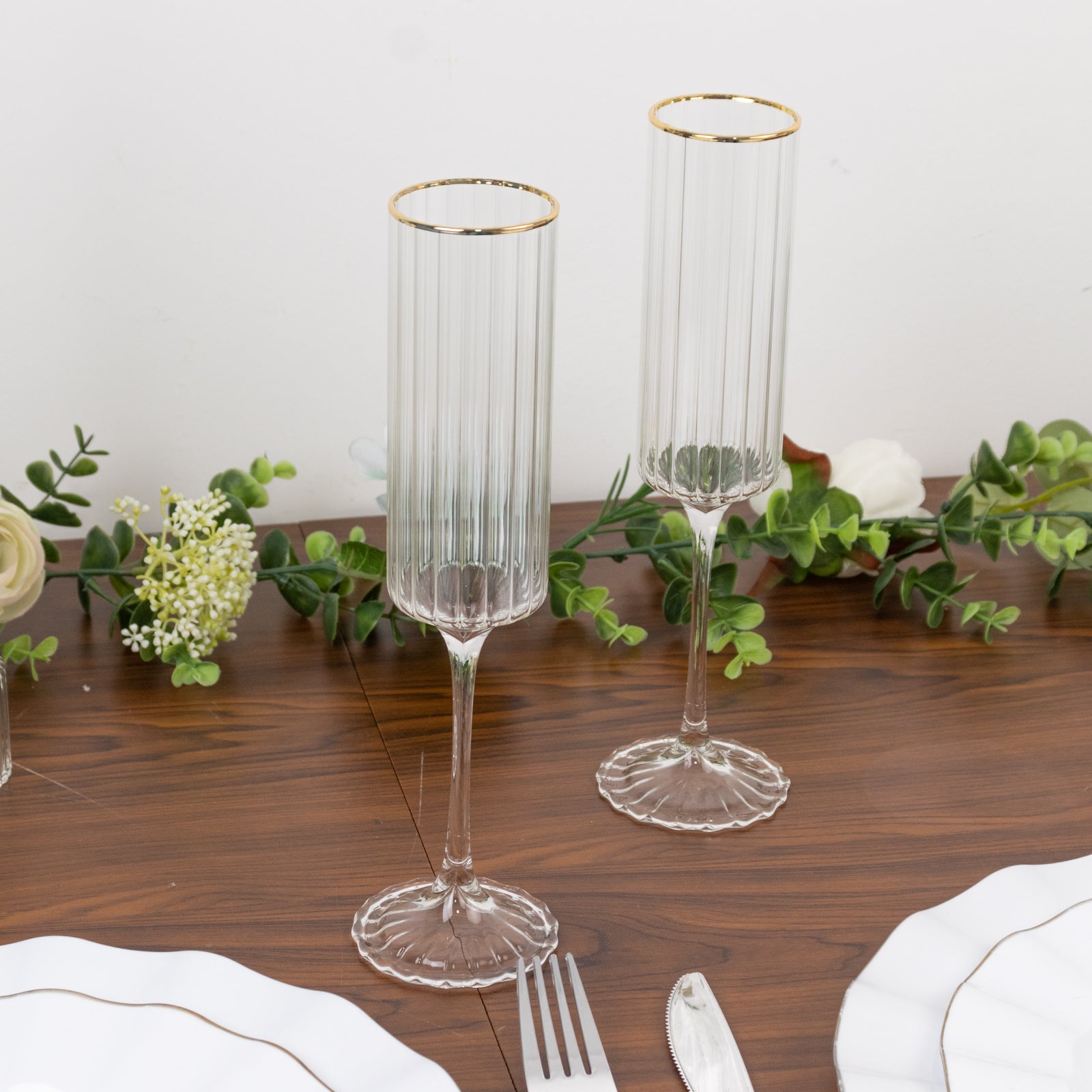 Clear modern champagne flutes with gold rim on a wooden table.