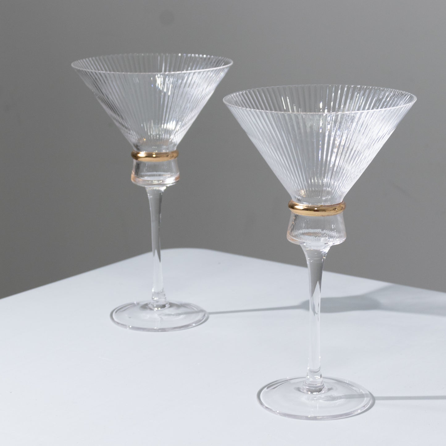 Clear martini glasses with ribbed design and gold ring accent, elegant for cocktails.