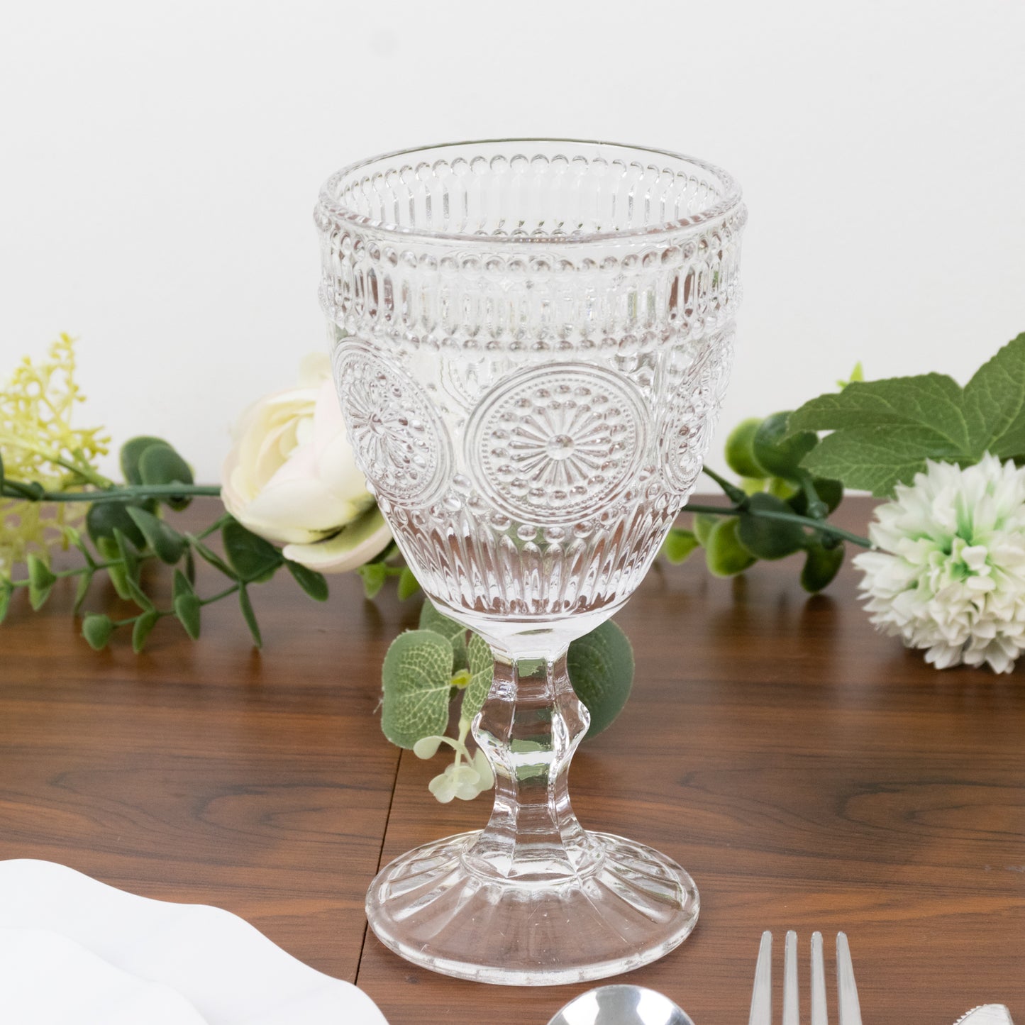 Clear vintage embossed goblet with floral design on a wooden table.