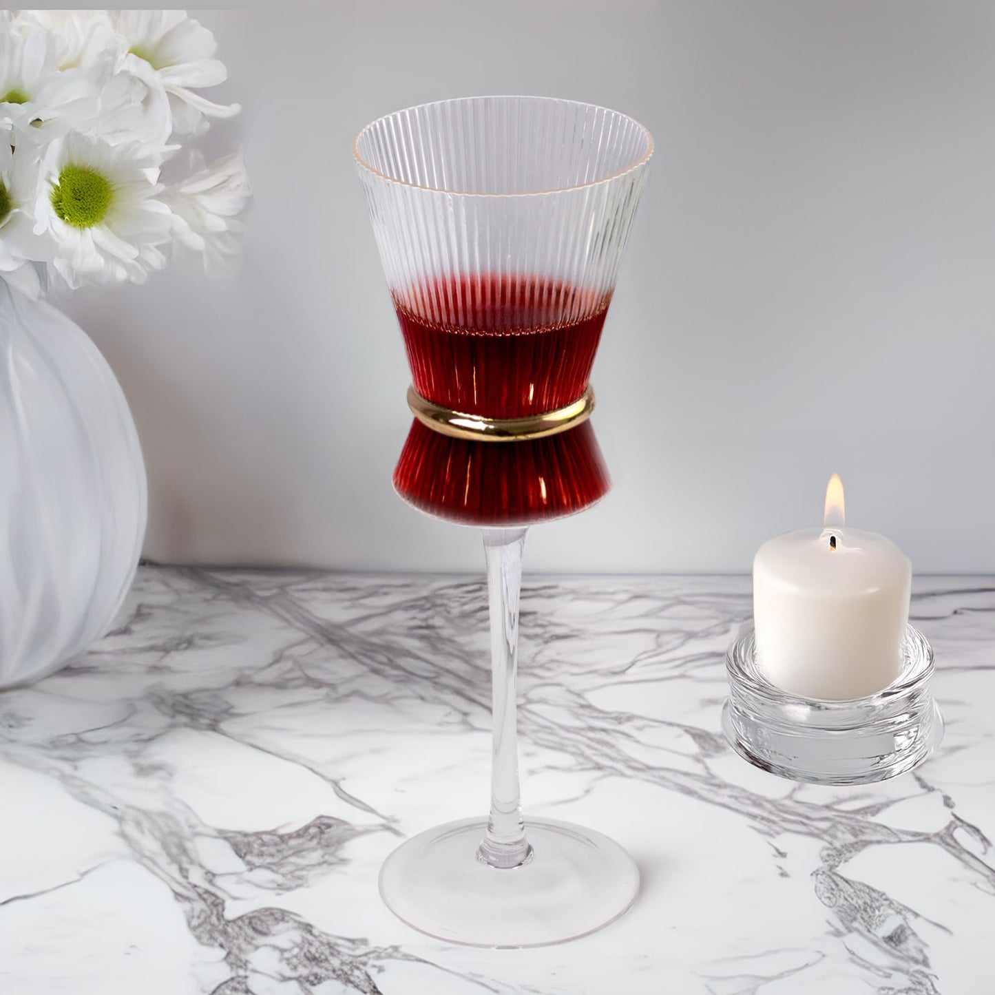 Clear wine glass with ribbed design and gold ring, filled with red wine.
