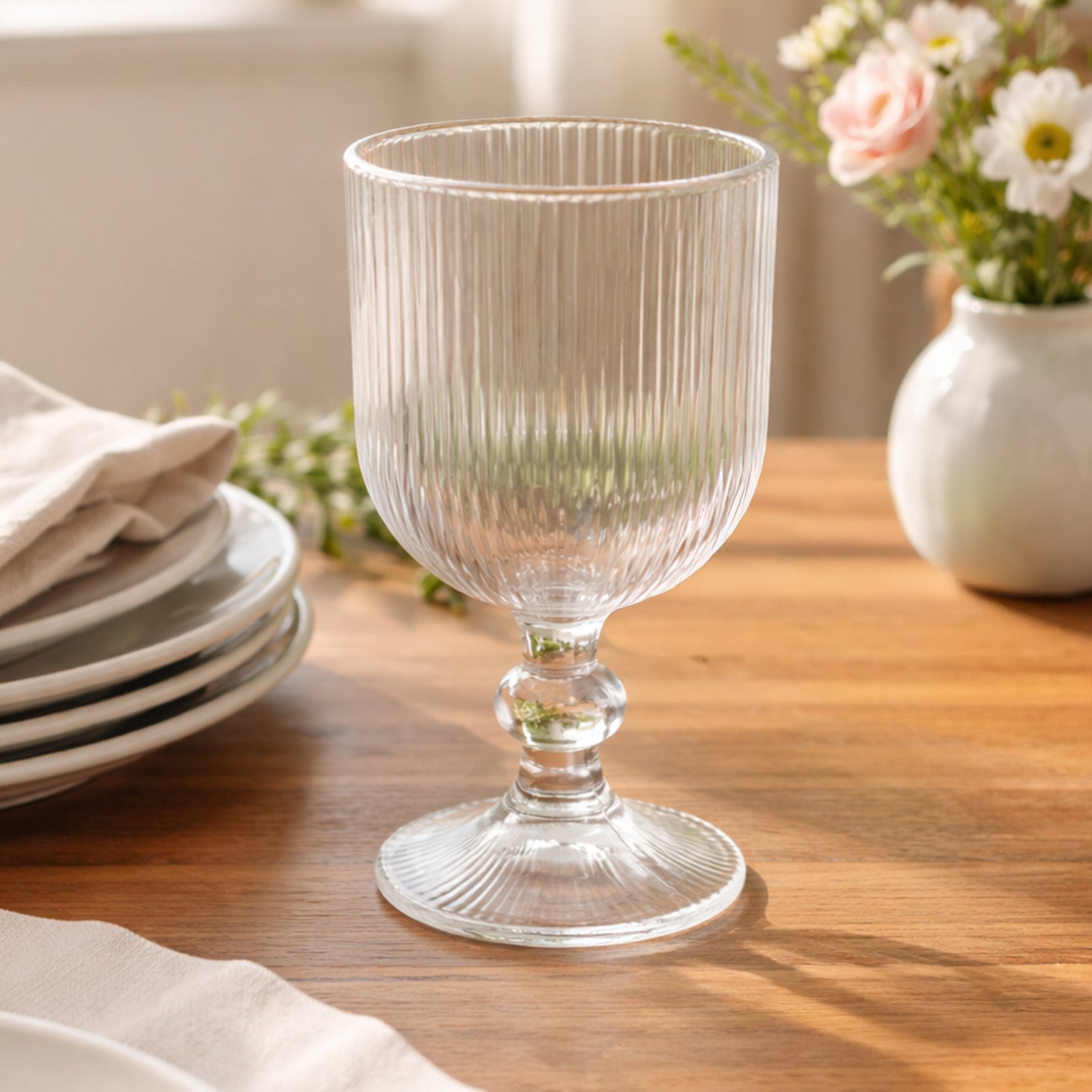 Clear ribbed wine glass on a wooden table with flowers.