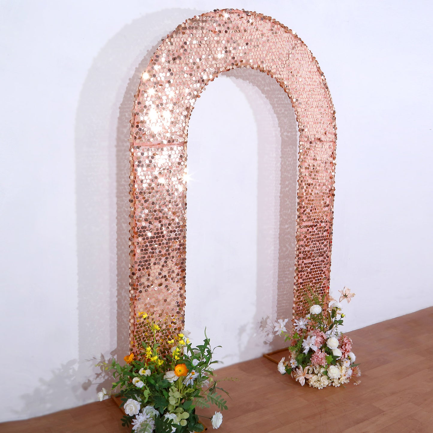 Rose gold sequin wedding arch with floral arrangements at the base.