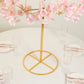 Gold metal umbrella flower stand with pink floral accents on a round base.