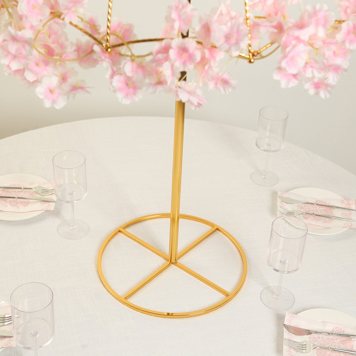 Gold metal umbrella flower stand with pink floral accents on a round base.