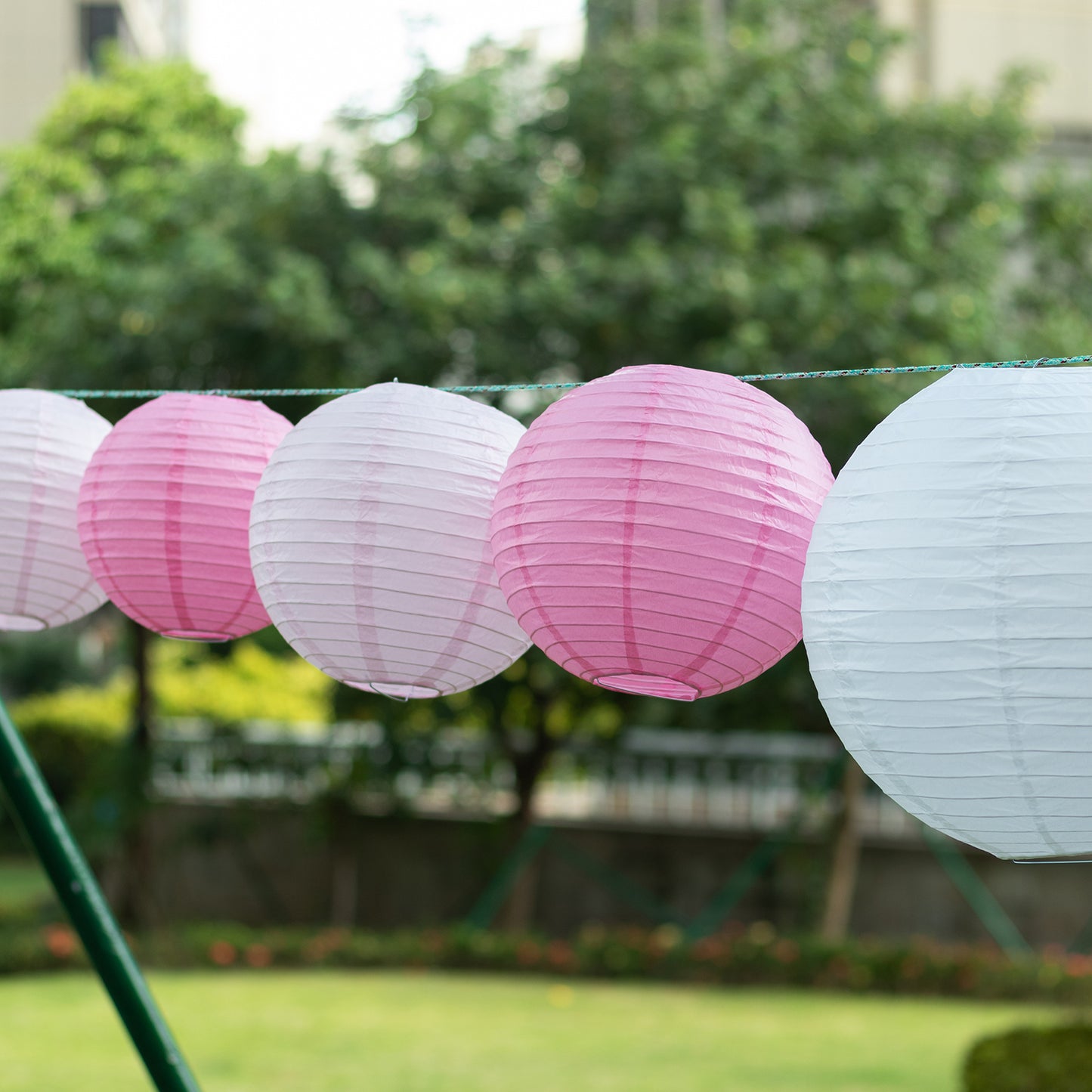 Set of 8 blush pink and white hanging paper lanterns in assorted sizes.