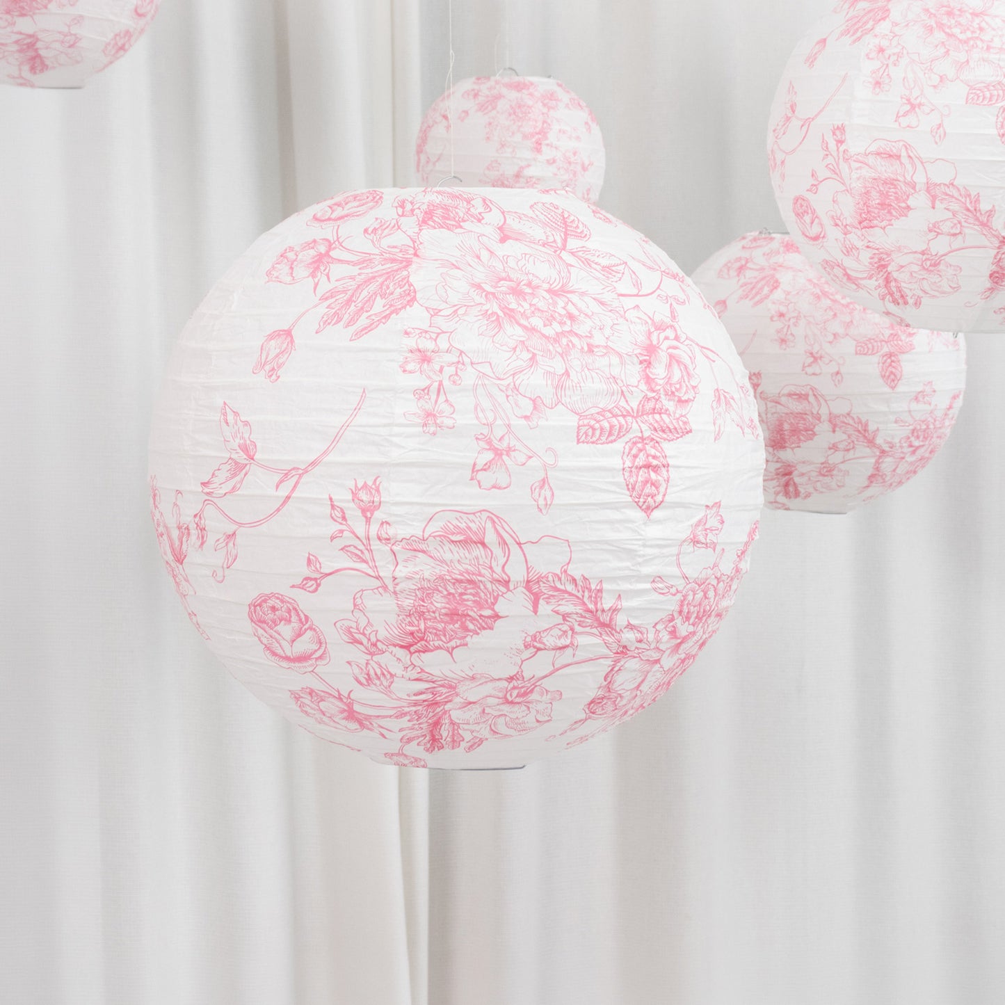 White paper lanterns with pink floral pattern, decorative hanging accents.