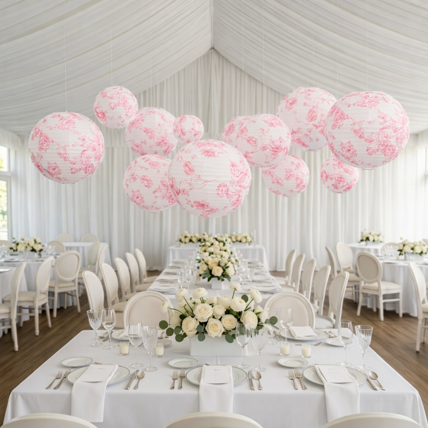 White paper lanterns with pink floral pattern hanging over a dining setup.