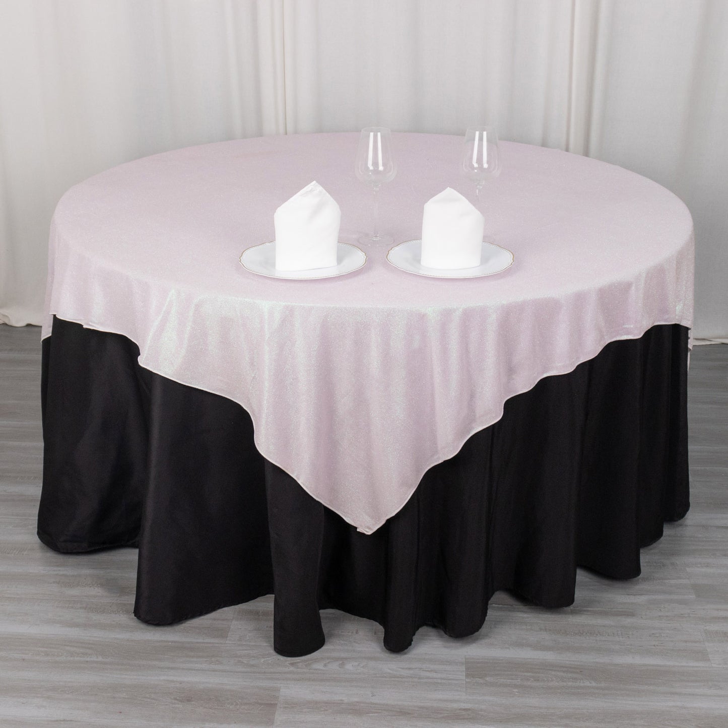 Iridescent pink glitter table overlay on a round table with black skirt.