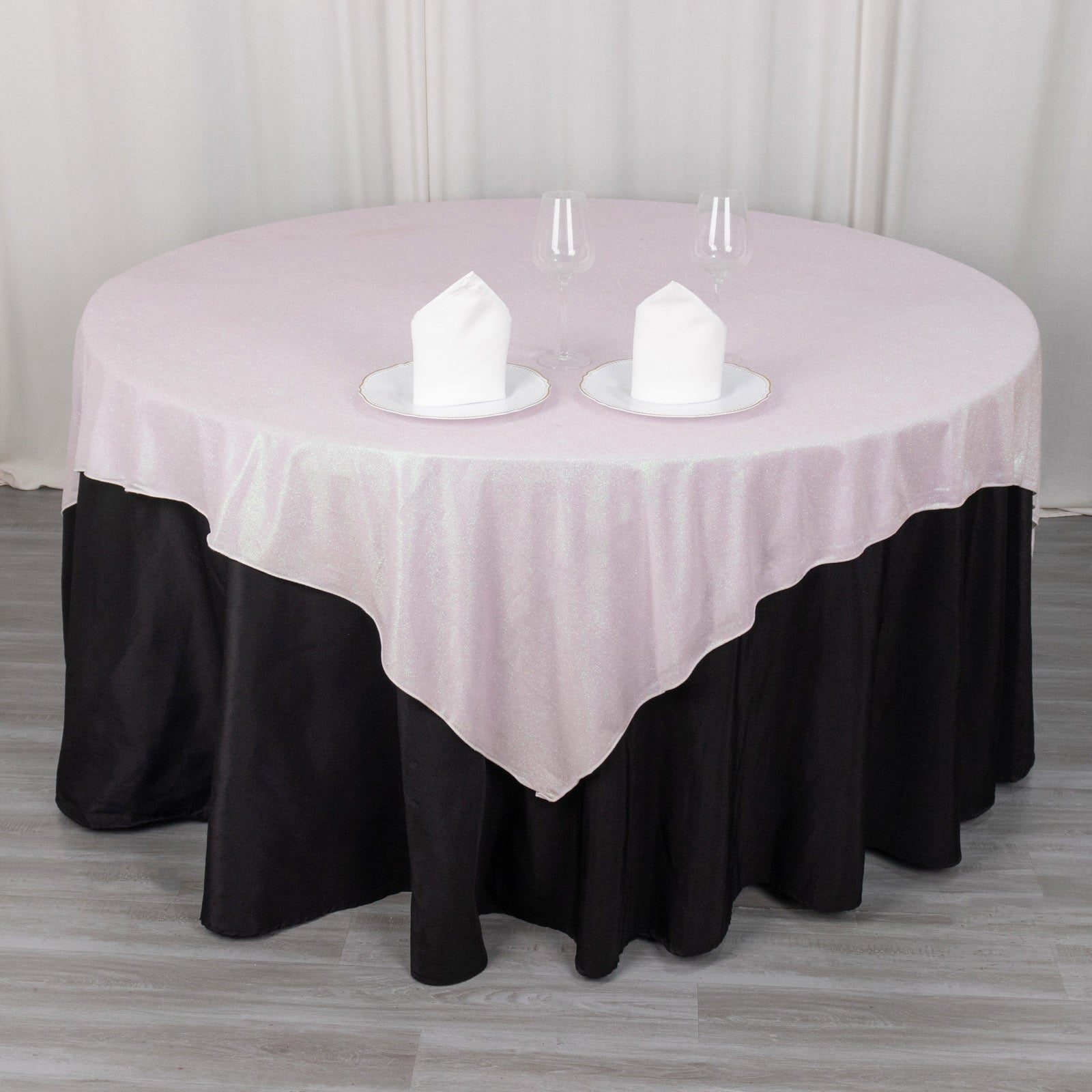 Iridescent pink glitter table overlay on a round table with black skirt.
