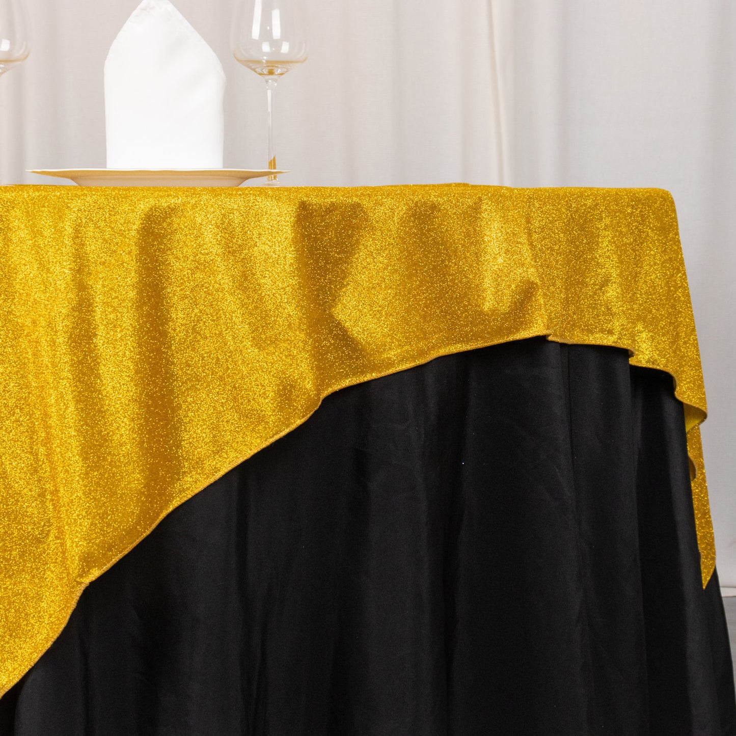Gold glitter table overlay on a black tablecloth, perfect for elegant events.