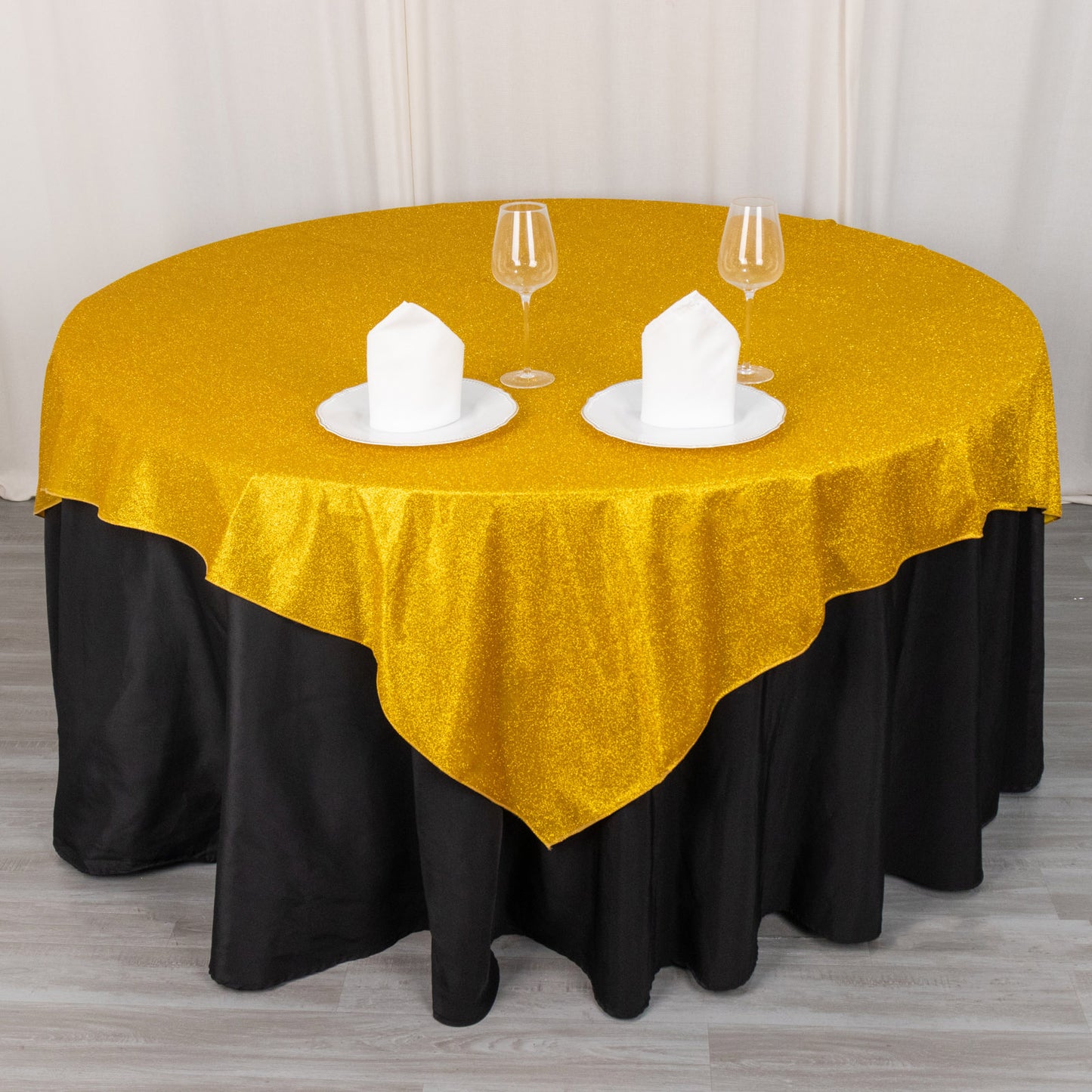 Gold glitter table overlay on a round black table with white plates and glasses.