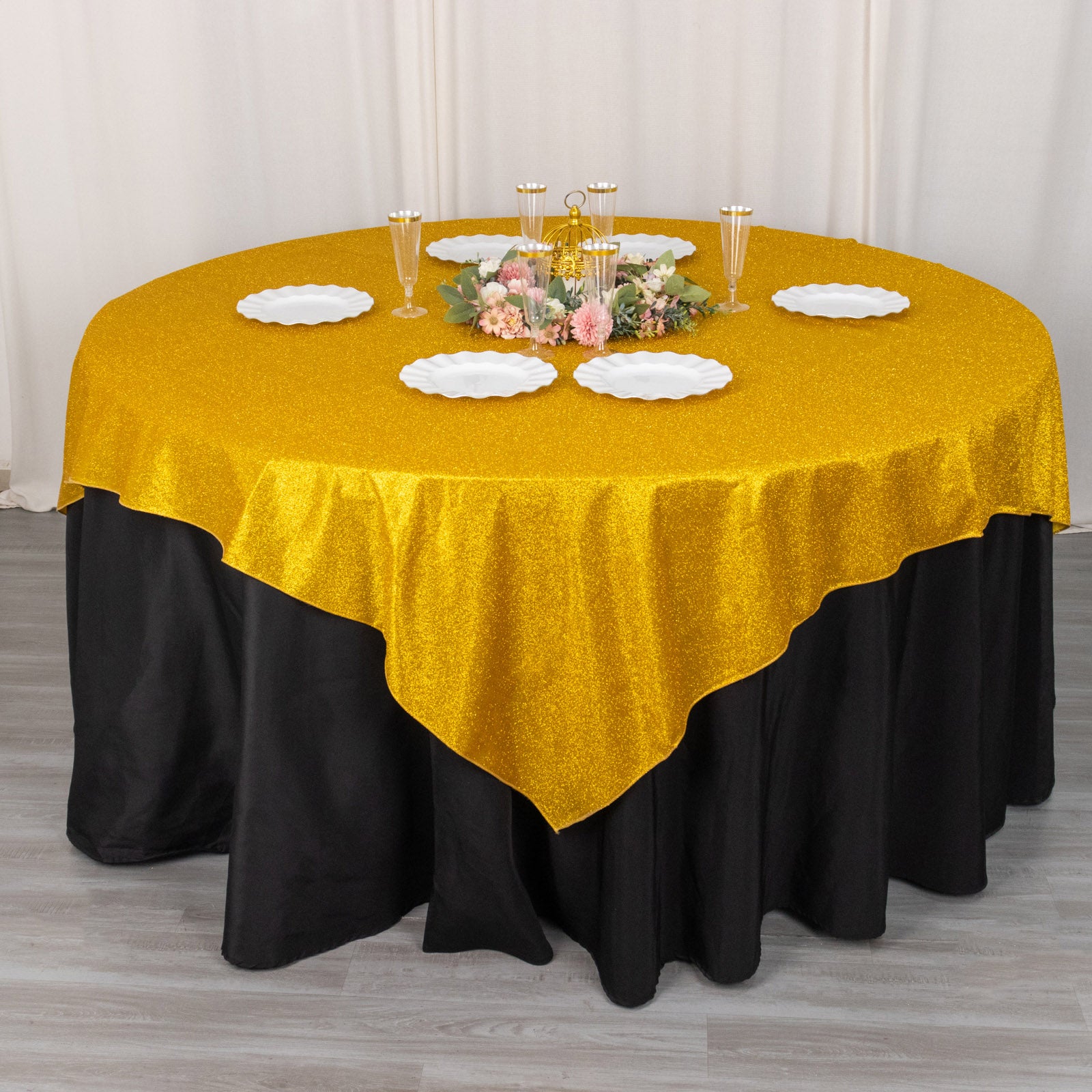 Gold glitter table overlay on a black tablecloth with floral centerpiece.