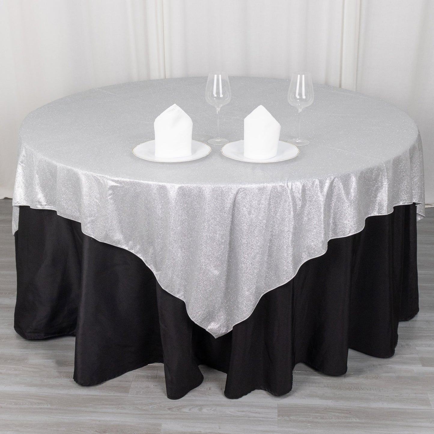 Silver glitter table overlay on a round table with black skirt.