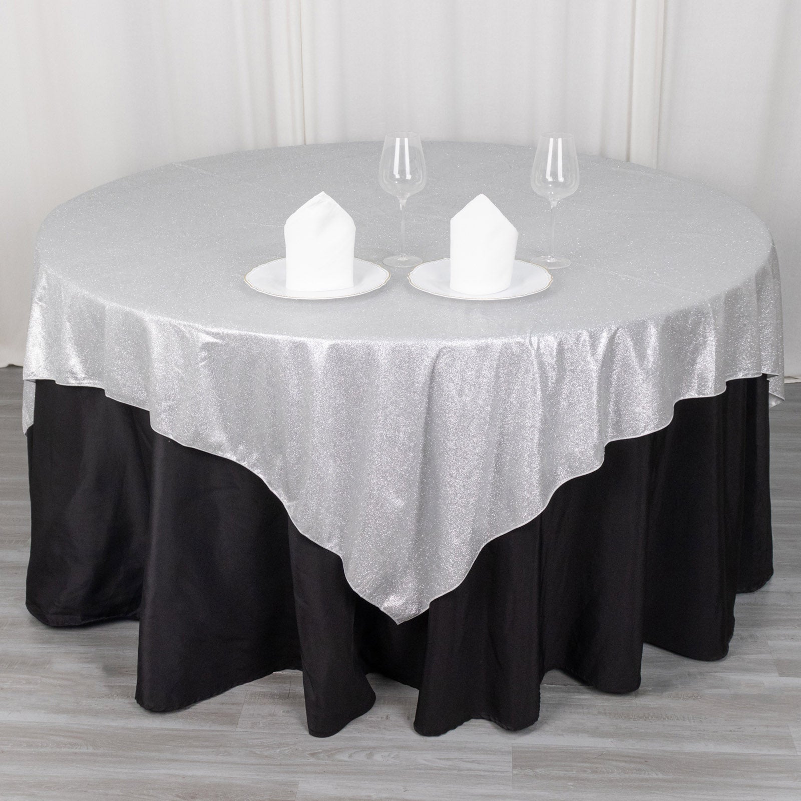Silver glitter table overlay on a round table with black skirt.