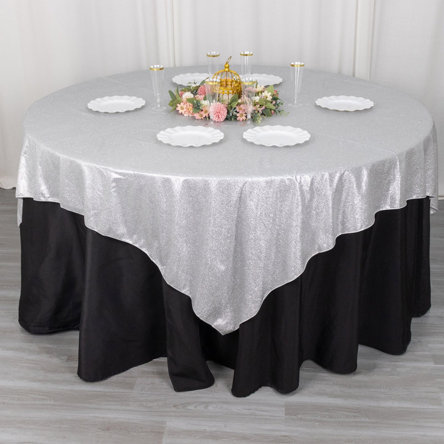 Silver glitter table overlay on a round table with floral centerpiece.