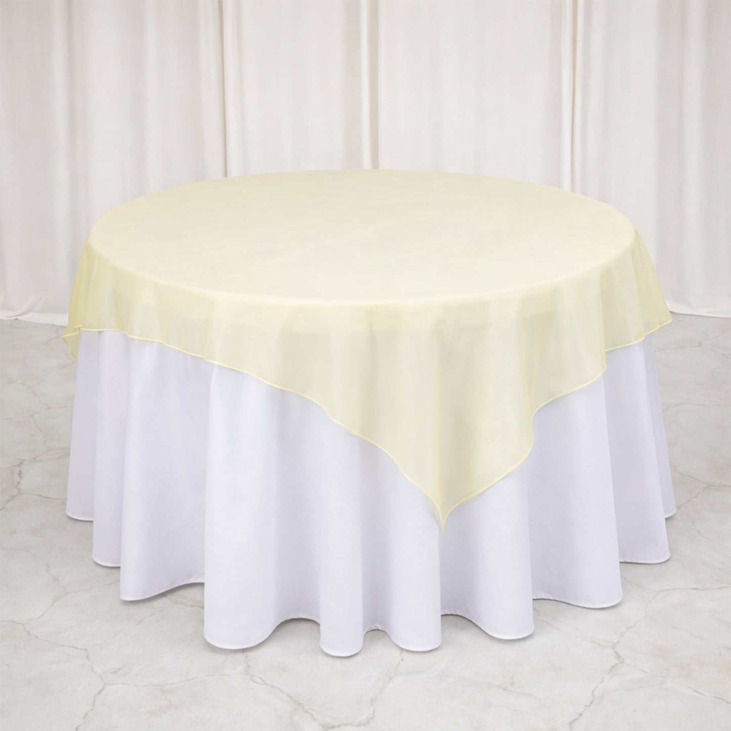 Champagne organza table overlay on a round table with a white tablecloth.